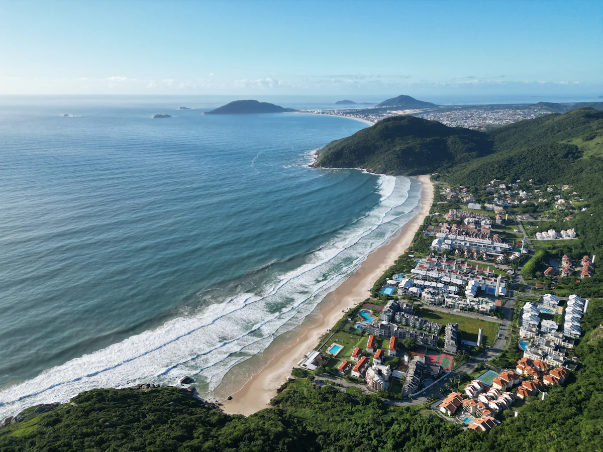 Playa de Florianópolis vista desde el aire, con cerros verdes y casas junto al mar