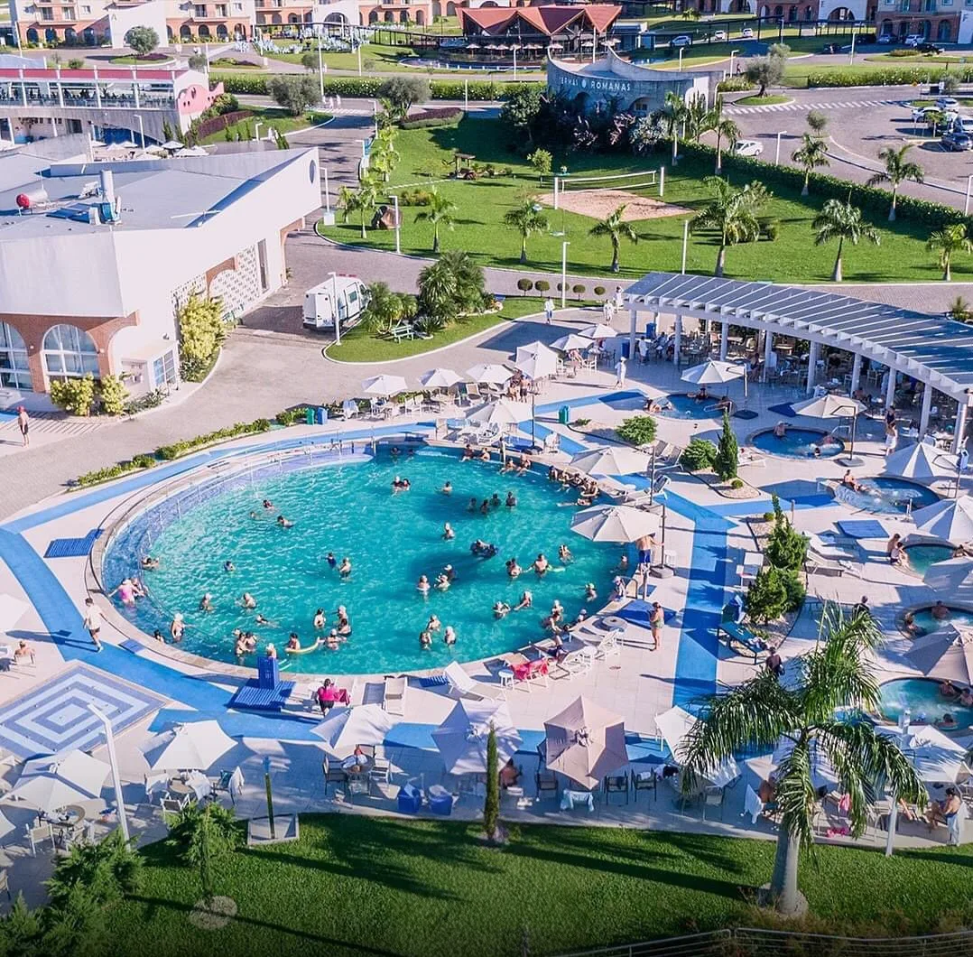 Vista aérea de la piscina del resort Termas Romanas, con sombrillas y palmeras