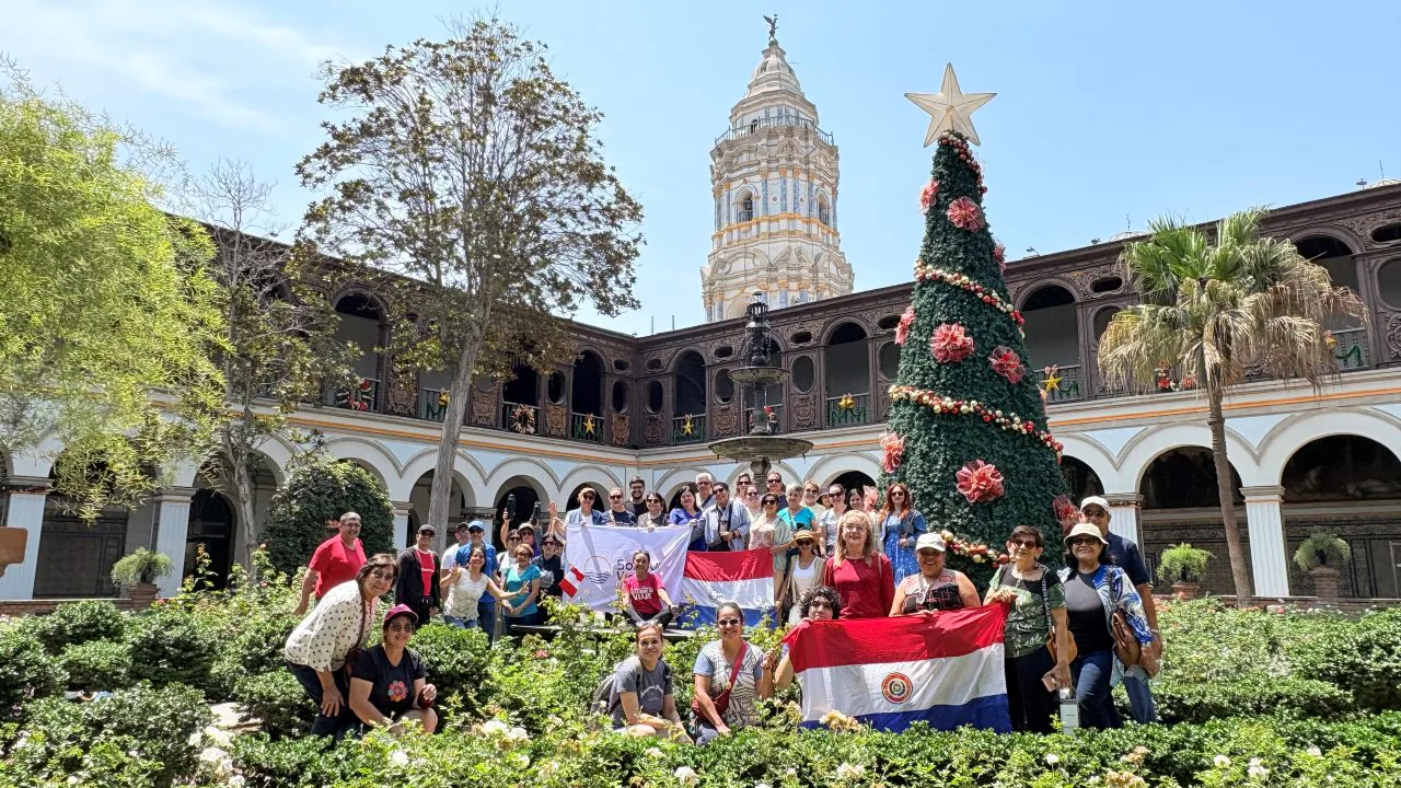Grupo de viajeros de Soltour con la bandera de la agencia, en un patio con jardines