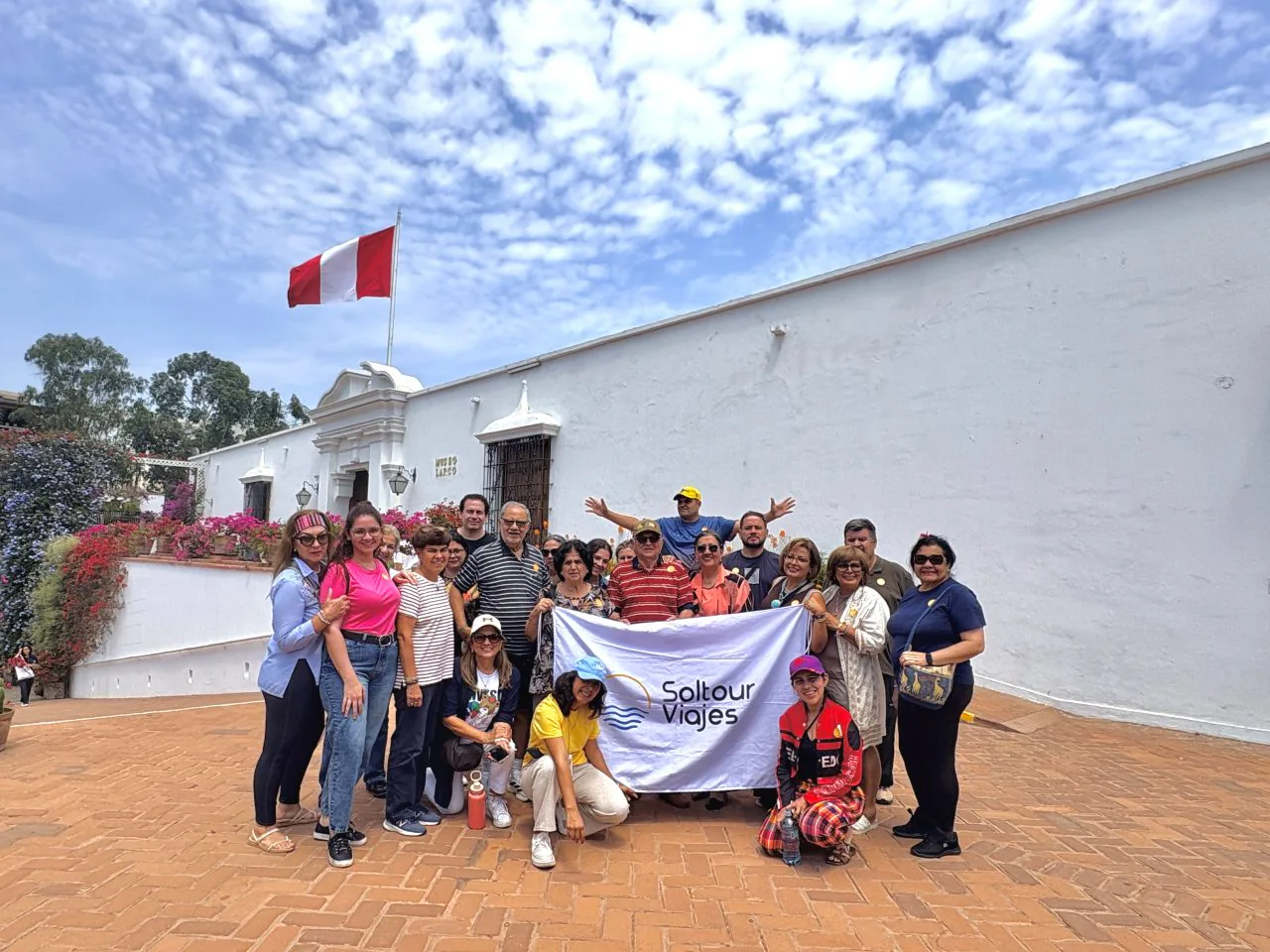 Grupo de viajeros de Soltour con la bandera de la agencia, frente a un edificio blanco