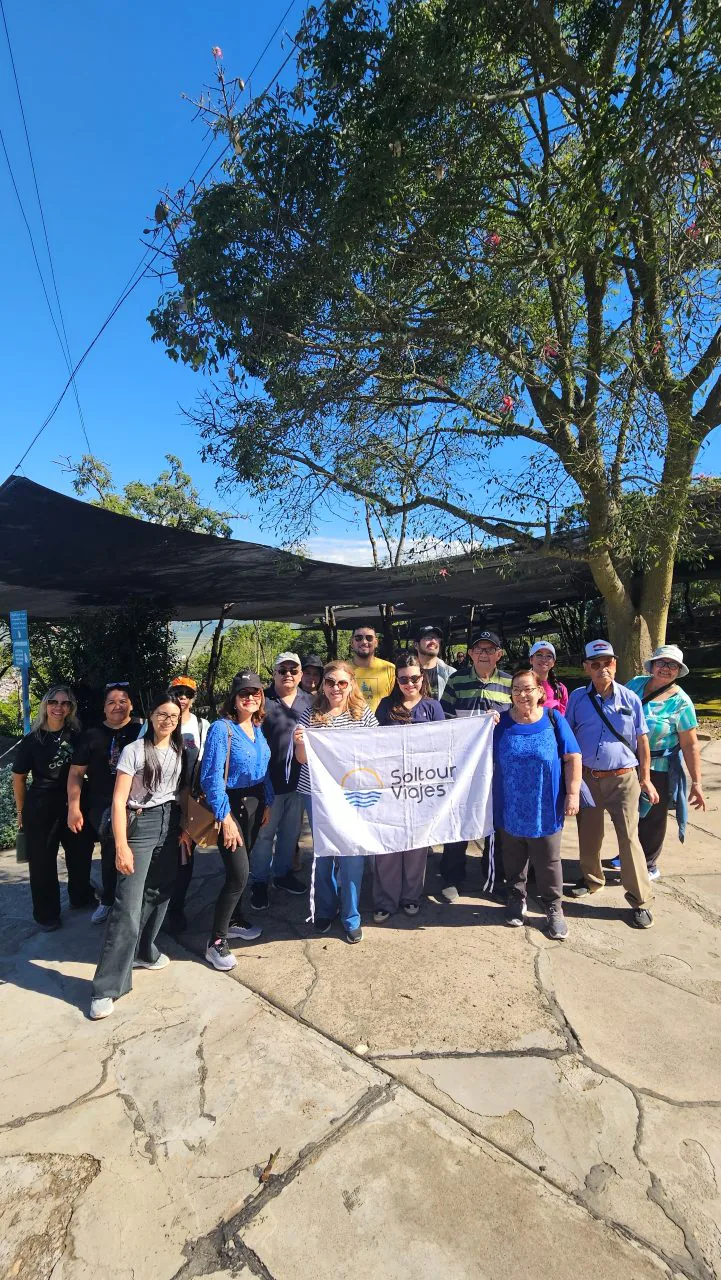 Grupo de viajeros de Soltour con la bandera de la agencia, bajo un árbol